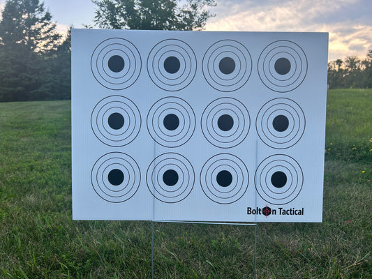 A white Bolton Tactical target stand with 12 circular bullseye targets, set up outdoors on a grassy field with trees and a sunset sky in the background.