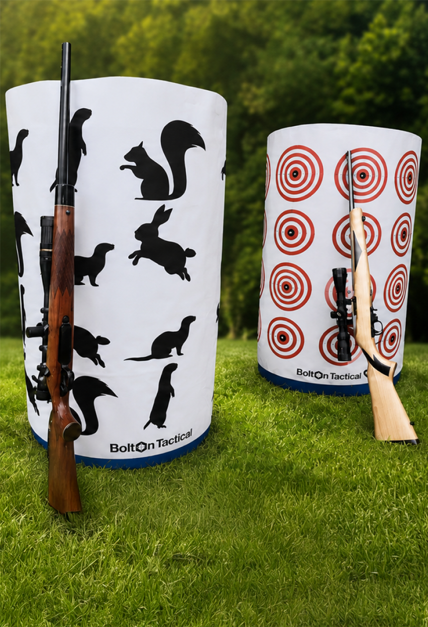 Two cylindrical Bullseye Target practice stands on a grassy field with a forest background. One stand is white with black animal silhouettes, and the other is white with red bullseye targets.